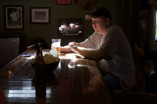A man in a Red Sox cap nursing a beer in the low light of a corner bar